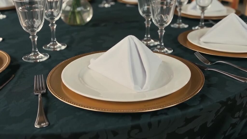 Mesa posta com sousplat dourado, prato branco e guardanapo dobrado para evento corporativo